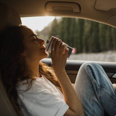 Jeune femme sereine dans sa voiture avec un café.